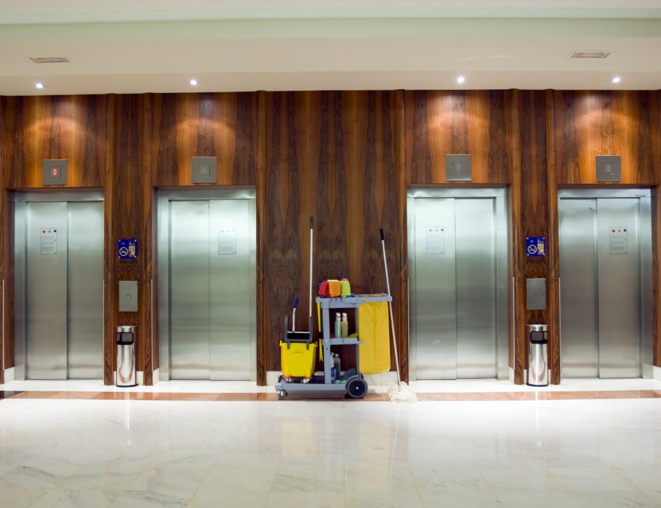 Cleaning cart in front of four closed elevator doors in a modern building lobby.